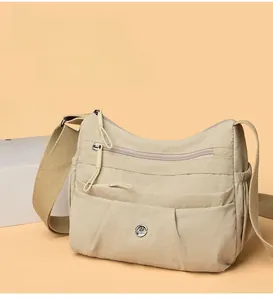 Detail view of the multi-layer zipper pockets and nylon texture on the beige crossbody bag
