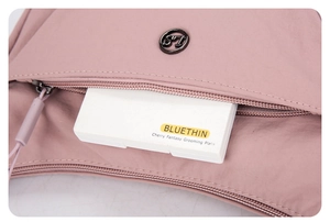 Détail de l'ouverture zippée du sac en nylon rose montrant une palette de maquillage
