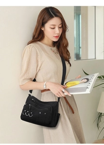 Detailed view of a multi-pocket black nylon crossbody bag worn by a model in casual attire