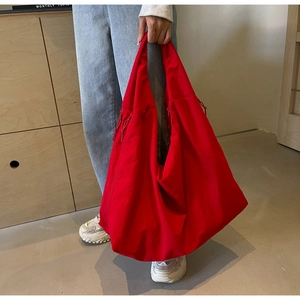 Detail view of large red canvas tote bag with side drawstrings held by a model