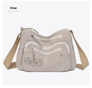 Detail of beige nylon crossbody bag with multiple zip pockets and metal ring accents