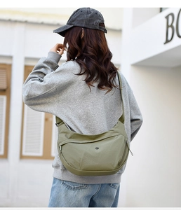 Outdoor shot of the olive green crescent bag worn by a model in casual grey casual wear