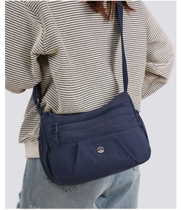 Close-up of a navy blue nylon crossbody bag with multi-layer zippers and metal logo