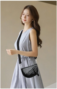 Detail of a black leather saddle bag with wide fabric strap and silver buckle on model