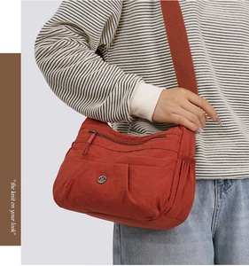 Close-up of a dark red nylon crossbody bag with multiple pockets and an M-shaped logo