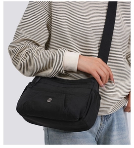 Side view of a multi-compartment black nylon crossbody bag worn by a model in casual style