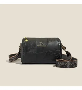 Detail of black patchwork cylinder bag with gold logo, wide strap and metal hardware