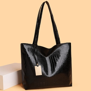 Stijlvolle zwarte shopper met krokodillenreliëf en gouden hanger op beige achtergrond