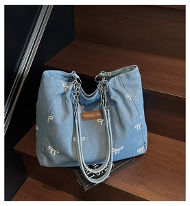 Detail of blue denim tote bag with white bow patterns and metal chain handle