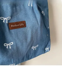 Close-up of blue denim tote bag with white bow patterns and brown leather logo patch