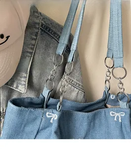 Detail of blue denim tote bag with bow embroidery and metal chain shoulder strap