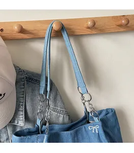 Close-up of denim tote bag with white bow embroidery and metallic strap rings