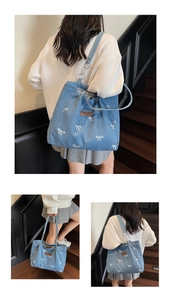 Detailed view of light blue denim tote bag with white bow prints and sturdy shoulder strap
