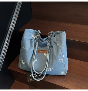 Detail of light blue denim tote with white bow prints and silver chain shoulder strap