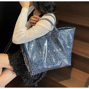 Detail of blue leopard tote bag with clear PVC overlay held by a model on stairs