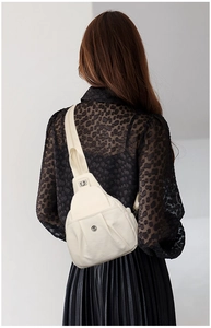 Detail of off-white leather chest bag with stylish pleats and metal logo on strap