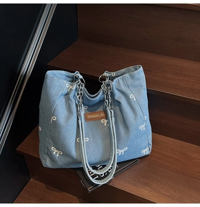Detail of light blue denim tote bag with white bow prints and metallic chain strap