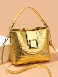 Detail of golden crocodile textured bucket bag with metallic buckle and detachable strap