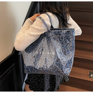 Detail of a large capacity blue leopard print tote bag worn on a woman's shoulder