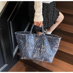 Detail of blue leopard print tote bag being carried by a model on dark wooden stairs