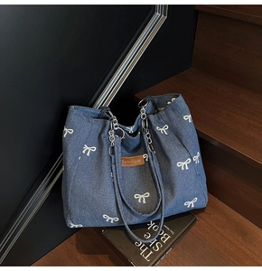 Detail of blue denim tote bag with white bow patterns and dual metal chain handles