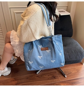Detail of blue denim tote bag featuring white bow prints and silver chain shoulder strap