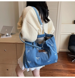 Detail of blue denim tote bag with white bow patterns and brown leather label