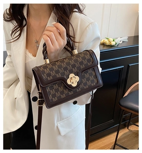 Brown handbag with M-pattern and gold flower clasp worn with a white blazer