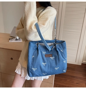 Detail of blue denim tote bag with white bow embroidery and brown leather label