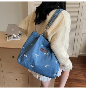 Detail of blue denim tote bag with white bow embroidery and silver metal chain strap