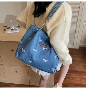 Detail of blue denim tote bag featuring white bow embroidery and metal chain strap