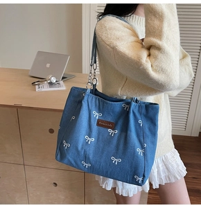 Detail of blue denim tote bag with white bow embroidery and metal chain shoulder straps