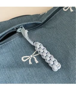 Detail der hellblauen Jeans-Tasche mit weißen Schleifen-Prints und geflochtenem Reißverschluss