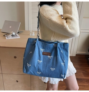 Detail of blue denim tote bag with white bow embroidery and metallic chain strap