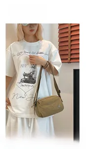 Close-up of a khaki nylon puff crossbody bag shown with a white casual graphic t-shirt