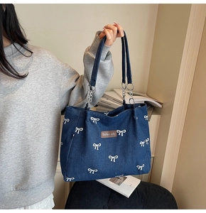 Detail of blue denim tote bag featuring white bow patterns and silver chain handles