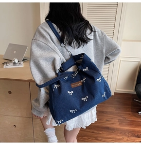 Detail of blue denim tote bag featuring white bow prints and brand logo on shoulder
