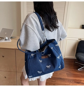 Detail of blue denim tote bag featuring white bow prints and vintage chain strap accents