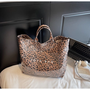 Leopard print tote bag with white text near laptop and headphones for commuting