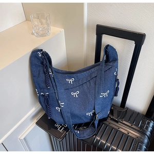 Detail einer blauen Denim-Tragetasche mit weißer Schleifenstickerei auf einem Koffer