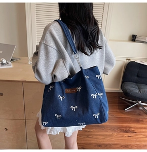 Detail view of denim tote bag with bow embroidery and metal chain strap on shoulder
