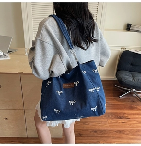 Close-up of blue denim tote bag with white bow print and brown leather brand label