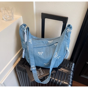 Detail der blauen Denim Hobo Bag mit weißem Schleifenmuster und gewebtem Reißverschlussanhänger