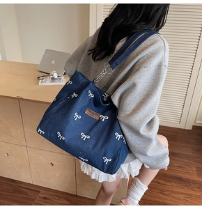 Detail of dark blue denim tote with white bow pattern and metal chain strap
