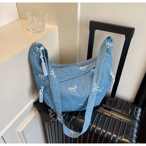 Detailansicht der hellblauen Jeans-Umhängetasche mit weißen Schleifen und gewebtem Anhänger