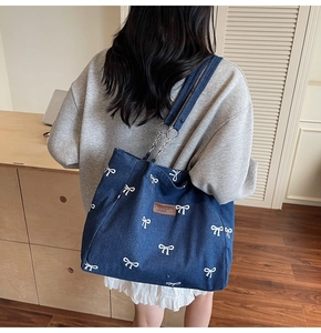 Detail of blue denim tote bag featuring white bow embroidery and silver chain strap