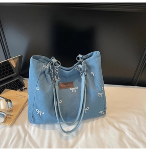 Detail of blue denim tote bag with white bow patterns and metal chain strap handle