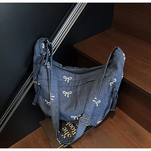 Detail der Denim-Umhängetasche mit weißen Schleifen-Stickereien und verstellbarer Schnalle