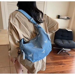 Makroaufnahme der Denim-Schultertasche mit weißen Stickereien und Metallschnalle