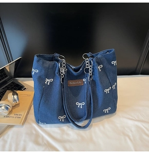 Detail of blue denim tote bag with white bow patterns and silver metal chain strap
